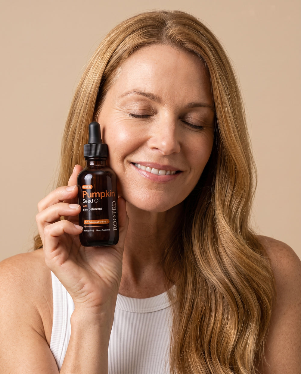 Woman holding a bottle of Rooted pumpkin seed oil drops to her cheek